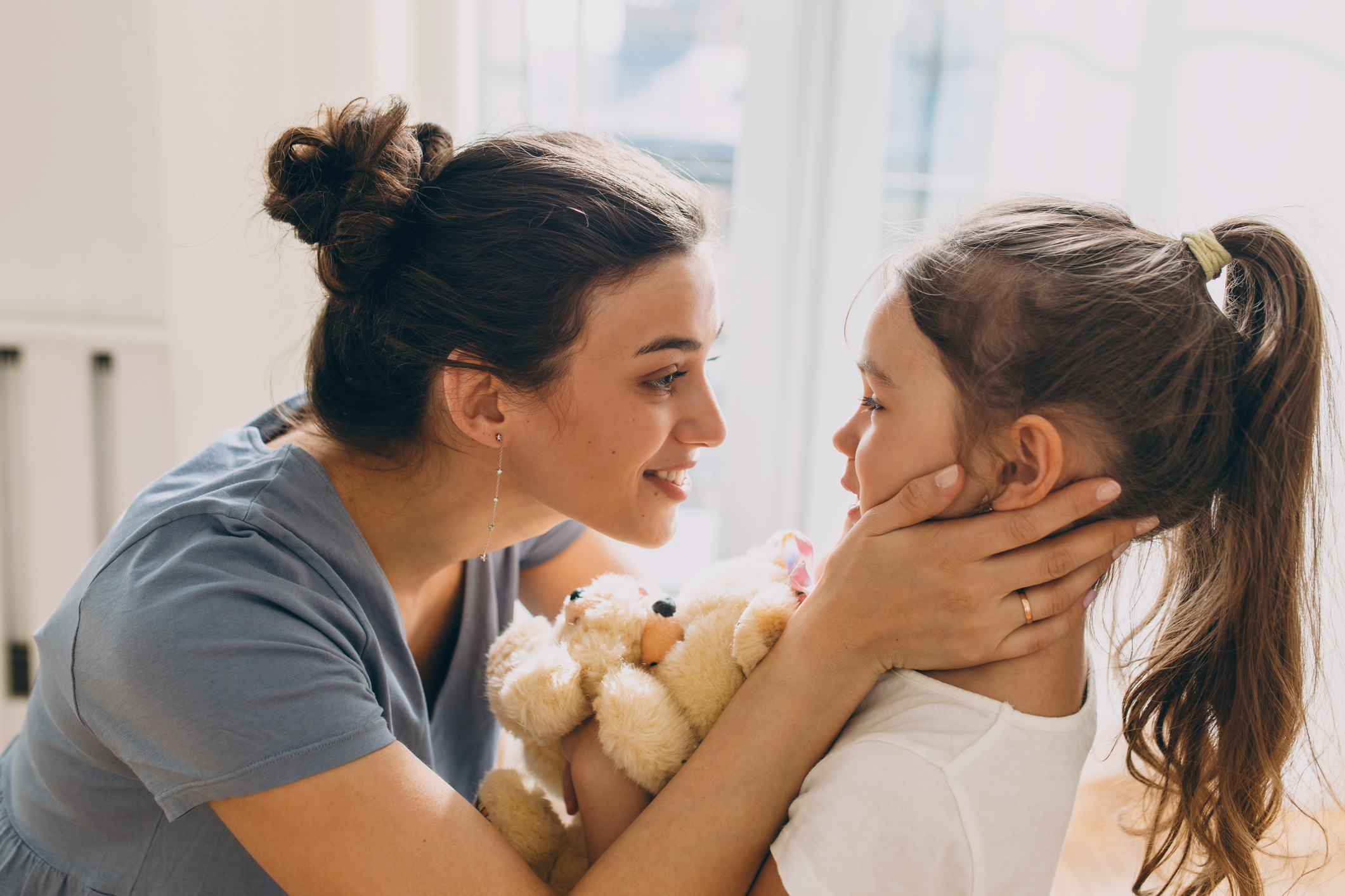 A mother holding her young daughter who is hugging a teddy bear